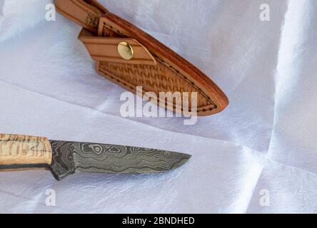 A fixed blade damascus knife and leather sheath displayed together on a white fabric. A beautiful set perfect for the advid hunter or collector. Bokeh Stock Photo