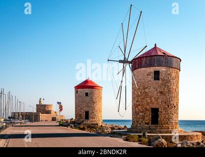 Situated on the long wave breaker at Mandraki harbour, Rhodes, Greece, stand these  medieval windmills. The fortress and the lighthouse of Agios Nikol Stock Photo