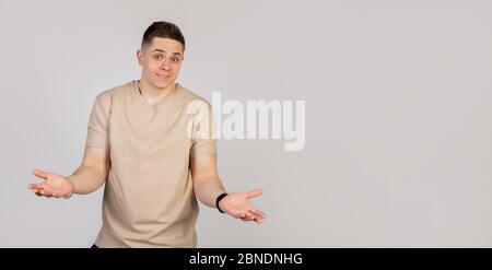 A handsome young guy a man smiles and shrugs spreading hands, does not know what to say in response. Language of the body. Looks at the camera. Stock Photo