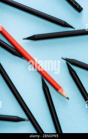 Top view of unique red pencil among black on blue background Stock Photo