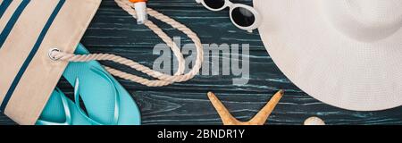 Panoramic shot of top view of sunglasses, flip flops near bag and starfish on dark wooden surface Stock Photo