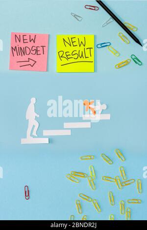 Top view of sticky notes with new mindset and new result lettering with paper clips, pencil and decorative men on career ladder on blue Stock Photo