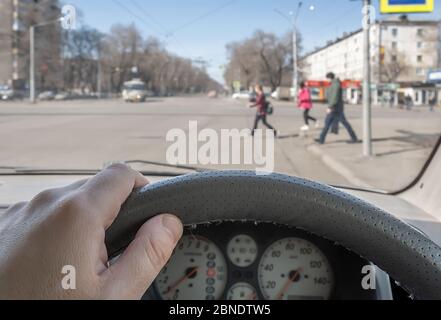 view from the car, the man's hand on the steering wheel of the car, located opposite the pedestrian crossing and pedestrians crossing the road Stock Photo