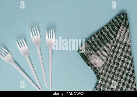 Four plastic forks and a linen kitchen towel on a light blue background. White disposable forks and a green plaid towel. Serving, food industry. View Stock Photo