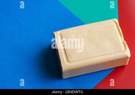 Laundry soap on a colorful background. A single rectangular piece of soap on a red-blue-green background. Demonstration of a single piece of new soap. Stock Photo
