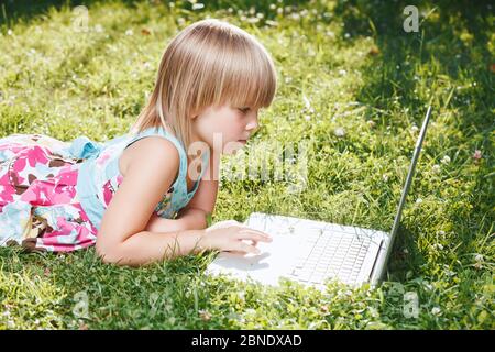 Little girl using laptop computer in a backyard. Child studying at home doing her homework or having online lesson. Homeschooling concept Stock Photo