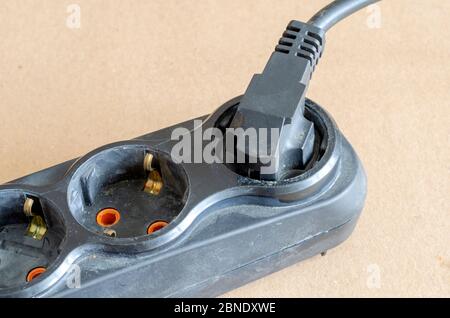 Used electric extension cord on a beige background. Black developer with a plug in the plug. Electrical Safety Rules. Close-up. Selective focus. Stock Photo