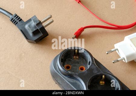 Black power strip with disconnected electricity consumers on a beige background. A developer with disconnected and randomly scattered various power pl Stock Photo