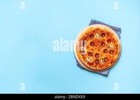 Tasty pepperoni pizza on a pizza stone, oven-fresh, on a blue seamless background. Flat lay with ready to eat pizza. Authentic Italian food. Stock Photo