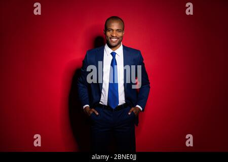 Portrait of his he nice attractive chic content cheerful guy ceo boss chief holding in hands in pockets posing trend isolated over red maroon burgundy Stock Photo