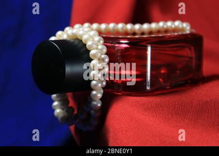 Red color men perfume bottle isolated on blue and red background with female accessories. Stock Photo