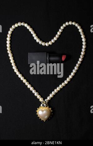 Red lipstick isolated on black background. Love heart design with white garland. Stock Photo