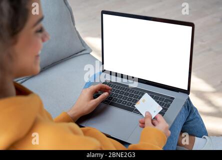 Happy hispanic female customer holding credit card paying online on laptop. Stock Photo