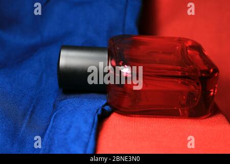 Red color men perfume bottle isolated on blue and red background with female accessories. Stock Photo