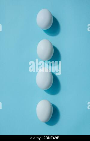 Four white eggs lie exactly in a row. They cast a shadow. Sharp edge of the eggs is directed in different directions. Stock Photo