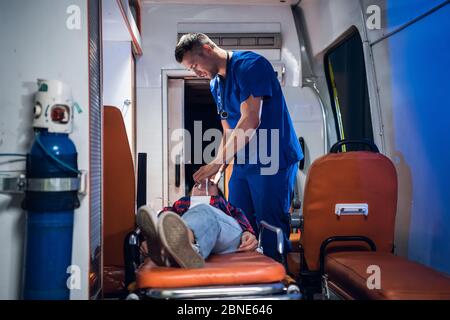 Young paramedic giving an oxygen mask to his female patient in an ambulance car Stock Photo