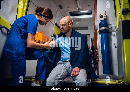 A female paramedic providing first aid to an injured man resqued from the fire, giving an injection Stock Photo
