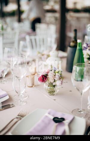 Wedding dinner table reception. A small glass case with rose flowers stands on the table in the form of decoration.  Stock Photo