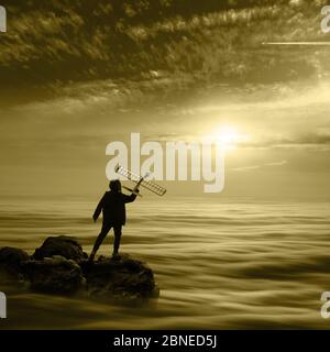Boy teenager is standing on the stone above cloud layer. He is going to launch to sky his model of airplane. Aircraft is flying high in the sky. Sunri Stock Photo