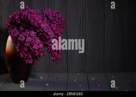 Bouquet of pink lilac flovers in vase on wooden table with fallen petals Stock Photo