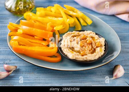 Close up of a bright yellow and orange paprika sticks with hummus on blue background Stock Photo