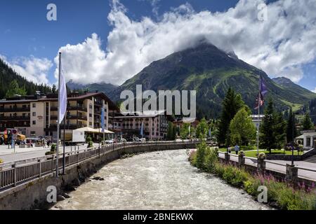 River Lech flowing alongside main street in Lech village, Vorarlberg, Austria. Omeshorn mountain summit in clouds. Stock Photo