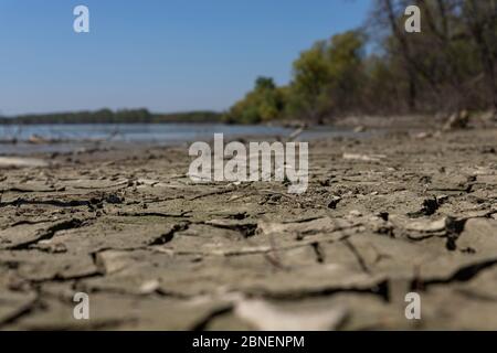 Cracked, muddy ground at the river bank with river Danube in background Stock Photo