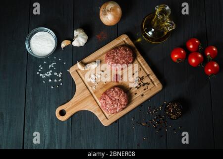 Cutlets from minced meat with the ingredients on the black wooden table. Home cooking. Stock Photo
