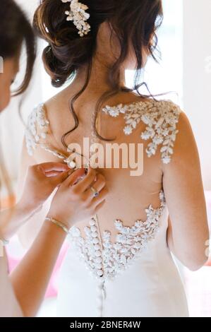 Bride's dress with white floral embroidery being buttoned up by bridesmaid Stock Photo