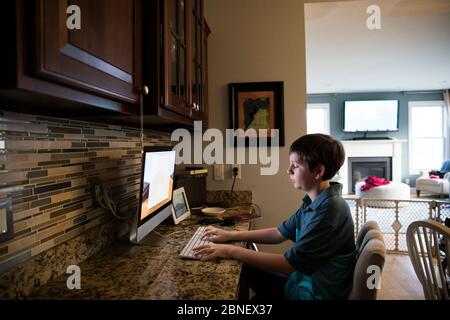 Wide View of Tween Boy Typing on Keyboard at Computer Desk Stock Photo
