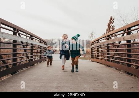 Siblings running together on bridge toward camera Stock Photo