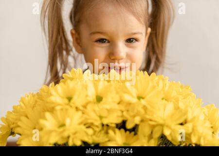 childhood, holidays, flowers, gifts concept - little cute three year old girl with two ponytails on her head in blue colorful dress holds large Stock Photo