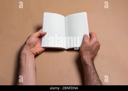 Male hands holding an opened note book-catalog with blank pages on brown background, mock-up series template ready for your design, pages selection pa Stock Photo