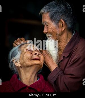 HOI AN, VIETNAM - Mar 14, 2018: An Asian couple with an old lady looking up at her husband while her husband is gently fixing her hair with black back Stock Photo