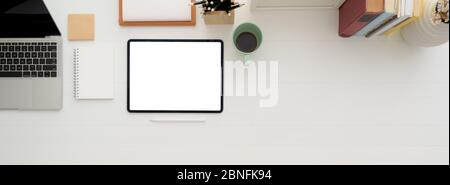 Overhead shot of minimal worktable with mock-up tablet, coffee mug, notebooks, stationery and copy space on white desk Stock Photo
