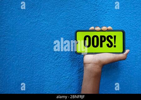 OOPS wording on smart phone screen isolated on blue background with copy space for text. Person holding mobile on his hand and showing front of the sc Stock Photo