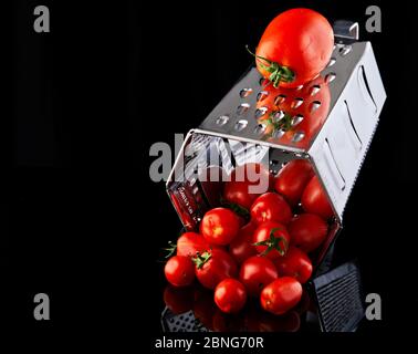 Culinary concept. Large tomato and grater down to small grape cherry tomatoes on a black background. Low calorie food Stock Photo