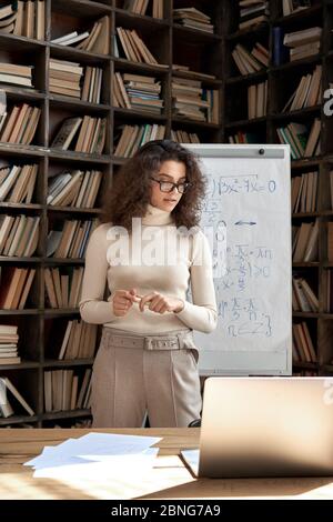 Hispanic woman teacher working in classroom with whiteboard and laptop. Stock Photo