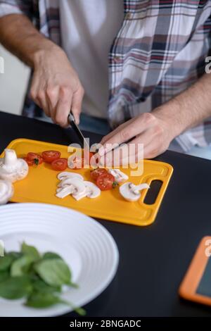 Male hands cutting cherry tomatoes and mushrooms. Stock Photo