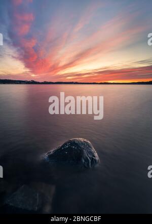 Scenic sunset with peaceful lake and rock at spring evening in Finland Stock Photo