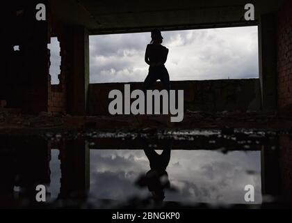 Silhouette of woman caucasian hip hop dancer, freestyling outdoors in an old abandoned building with refelection in puddle Stock Photo