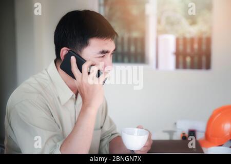 The young architect is talking on the phone with customers in his home office.  Concept Work from home. Stock Photo