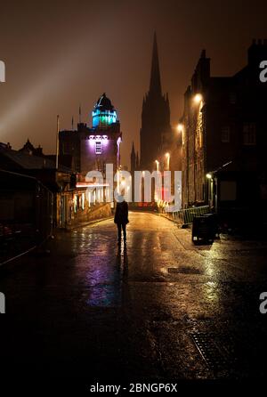 Beautiful foggy wet view of the Royal Mile in Edinburgh, Scotland, on a rainy winter night with a woman's silhouette and reflection of the lights Stock Photo
