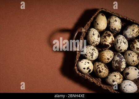 Quail egg in basket on brown background. Quail eggs. Happy easter concept. Minimal design. Copy space, flat lay, from above. Stock Photo