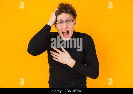 Image of young scared man in eyeglasses screaming and expressing surprise isolated over yellow background Stock Photo