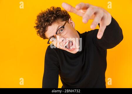 Image of young scary man screaming and reaching her arm forward at camera isolated over yellow background Stock Photo
