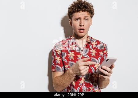 Image of young confused man using and pointing finger at cellphone isolated over white background Stock Photo