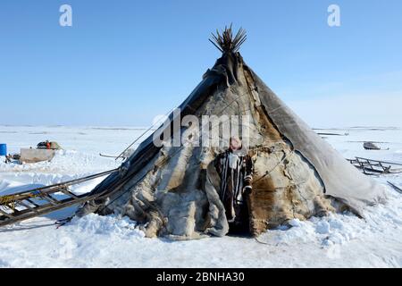 Carolina Serotetto, Nenet teenager standing at entrance of her reindeer fur covered tent, warmly dressed in traditional coat. Yar-Sale district. Yamal Stock Photo