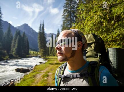 Portrait of hiker with big backpack and sunglasses near the river mountain valley in Karakol national park, Kyrgyzstan Stock Photo