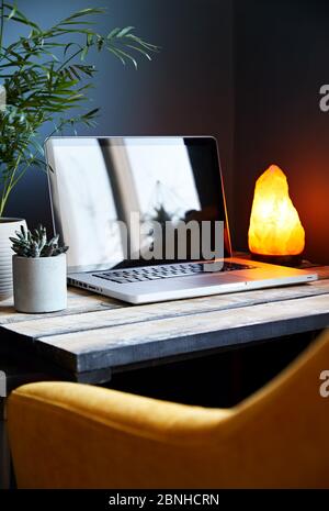 Cozy workspace with laptop yellow glowing lamp and chair at stone grey wall background. Working from home concept. Stock Photo